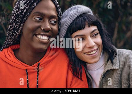 Close up portrait of two happy multi-ethnic women smiling with heads touching outdoors in a park. Stock Photo