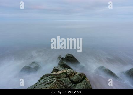 Stratified cliff rocks in Ireland with swirling sea, high-angle view, ethereal waves, minimalist seascape Stock Photo