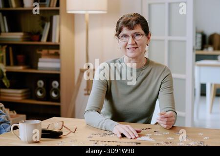 Portrait of Middle Aged Woman Assembling Puzzle at Table Indoors Stock Photo