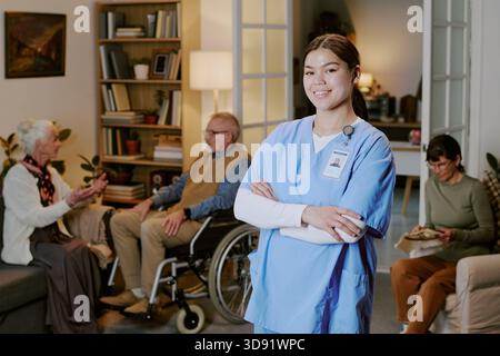 Young Adult Hispanic Woman Nurse Smiling While Standing in Senior Care Facility Stock Photo
