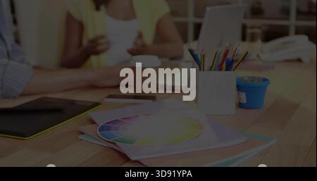 Showing color wheel resting on folders at wooden table, pencil cup and woman in yellow cardigan Stock Photo
