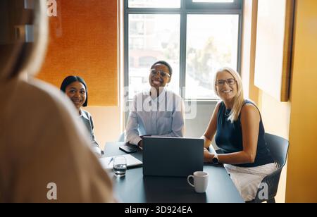 Three professionally-dressed businesswomen smiling during a business meeting in a sunlit office environment. The image conveys teamwork, positivity, a Stock Photo