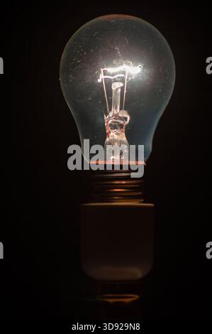 Glowing incandescent light bulb with visible filament isolated on black background. Stock Photo