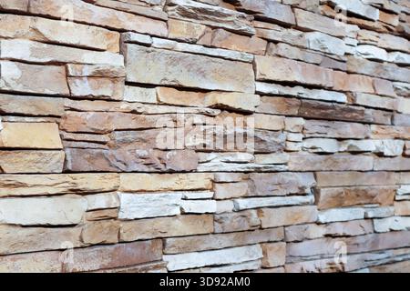 Detailed view of a natural stone wall with stacked beige and brown blocks, highlighting irregular shapes and textured surfaces in earthy hues. Stock Photo