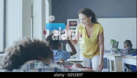Leaning teacher in yellow blouse white pants high-fiving boy in class right side, desk, copy space Stock Photo