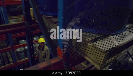 Inspecting worker wearing yellow hard hat, khaki vest scanning racks in storage, drums, copy space Stock Photo