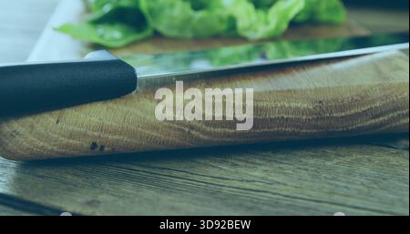 Showing wooden cutting board grain on wooden tabletop, with metal knife black handle and greens Stock Photo