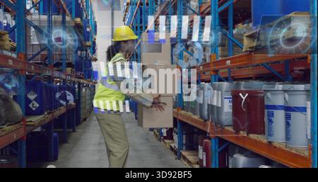 Carrying warehouse worker in hard hat and safety vest walking aisle, holding stacked boxes, AR HUD Stock Photo