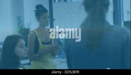 Standing woman in yellow overalls addressing team in open office, monitors and sticky notes Stock Photo
