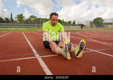 Senior athlete taking a break on track and field, stretching legs after intense training session Stock Photo