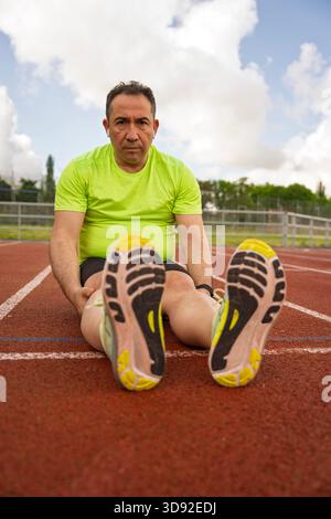 Senior athlete taking a break and stretching his legs on a running track after a workout Stock Photo