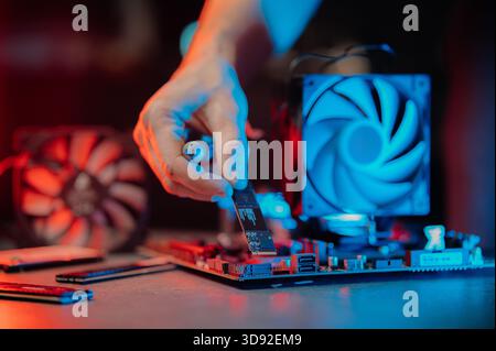 system administrator installing SSD into motherboard, assembling PC of different accessories or components, close-up view of hands, computer repair Stock Photo