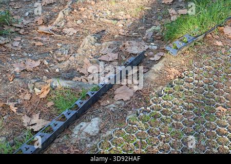 Close-up of durable black plastic lawn edging installed on soil border with permeable grass pavers and autumn foliage Stock Photo