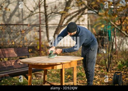 Man carpenter using sander on wood during furniture renovation outdoors Stock Photo
