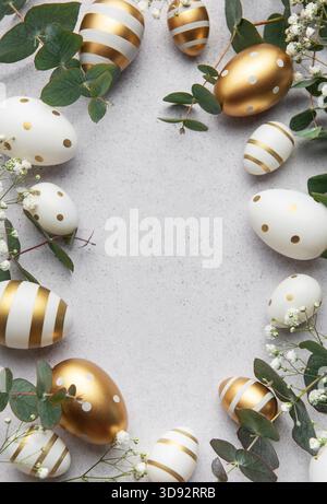 Easter eggs forming a frame with eucalyptus leaves and white flowers on a gray background Stock Photo