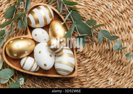 Easter decor. Easter eggs painted in gold in a heart-shaped wooden bowl. The concept of preparation for the celebration. Stock Photo