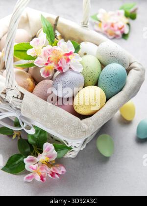Colorful easter eggs and spring flowers overflowing from a white wicker basket on a light background Stock Photo