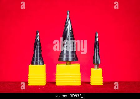 a set of conical step drill bits in various sizes on red at horizontal composition Stock Photo