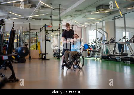 Man athlete in wheelchair working out with medicine ball at training session with professional coach Stock Photo