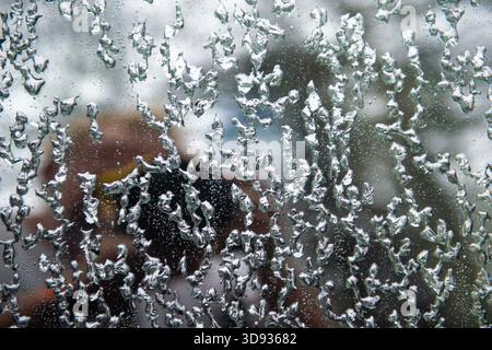 A window with frost and ice on it and a person's reflection in it. The reflection is blurry and the frost is intricate and detailed Stock Photo
