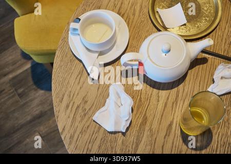 Leftover cup, teapot, and crumpled napkins on wooden table after afternoon tea. Stock Photo