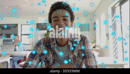 Smiling male student wearing plaid shirt leaning on desk in classroom, showing blue hex overlay Stock Photo