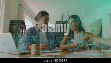 Reviewing paperwork, couple sitting at home dining table, using open laptop with teal data overlay Stock Photo