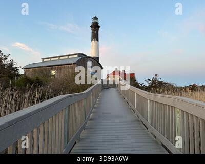 Wooden boardwalk leading to a coastal lighthouse on Long Island, New York, on a bright clear day by the shoreline. Stock Photo