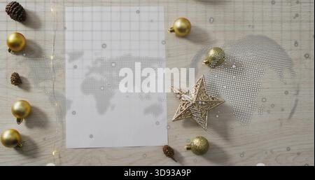 Displaying sheet showing dotted world map on light wood tabletop, with gold baubles, glittery star Stock Photo