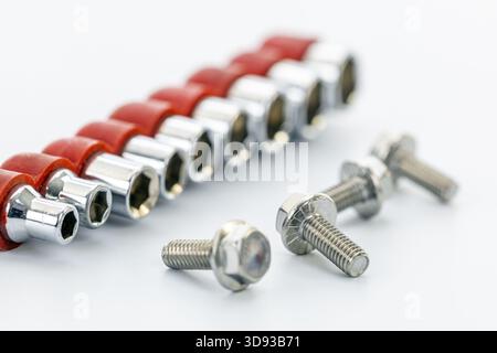 A set of chrome socket wrench heads with red holders arranged in a row on a white surface with three metal bolts in the foreground, showcasing tools f Stock Photo