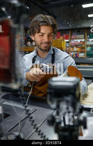 A man cashier wearing an apron is actively using a barcode scanner to scan a candle Stock Photo
