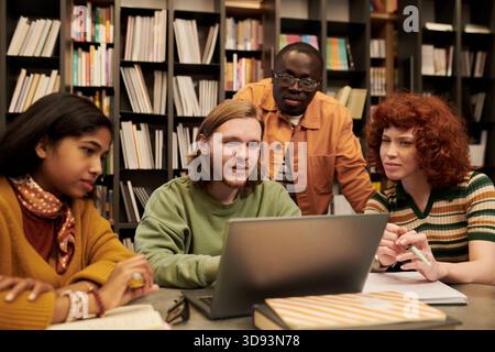 Diverse Young People Collaborating on Project in Library Setting Stock Photo