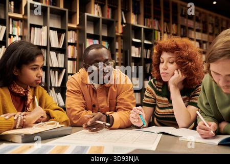Diverse Young People Collaborating on Project in Modern Library Setting Stock Photo