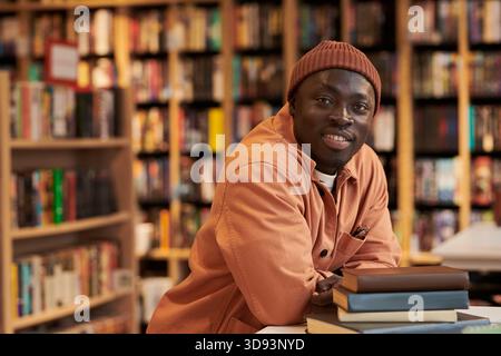 Portrait of Young Black Man Smiling While Leaning on Stack of Books Stock Photo