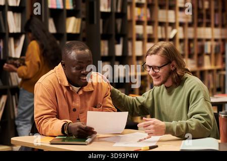 Young Black Man and Man Reviewing Documents and Smiling Together Stock Photo