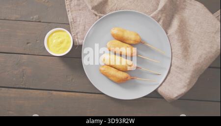 Presenting plate with four skewered corn dogs on dark tabletop, with mustard bowl and linen napkin Stock Photo