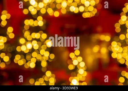 Blurred golden gift box with a red ribbon sits among small decorated Christmas trees with glowing fairy lights Stock Photo