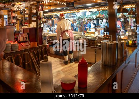 Lubeck, Germany - December 2, 2025: Grill stand for sausages and meat dishes at the Christmas market, staff from behind in appropriate clothing, selec Stock Photo