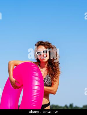 Happy curly woman relaxing on tropical beach with pink swim ring. Summer holiday. Stock Photo