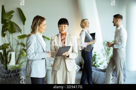 Two women and two men engage in a collaborative discussion in a contemporary office. The setting features plants and a relaxed atmosphere, promoting t Stock Photo