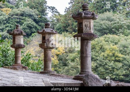 Three stone lanterns (Kasuga-dōrō) on a stone wall within the grounds of a shrine in Odawara, Kanagawa Prefecture, Japan. The Kasuga style, with its hexagonal lampshade and characteristic curved roof (kasa), is one of the most common types of lantern found in Shinto shrines and Buddhist temples across Japan Stock Photo