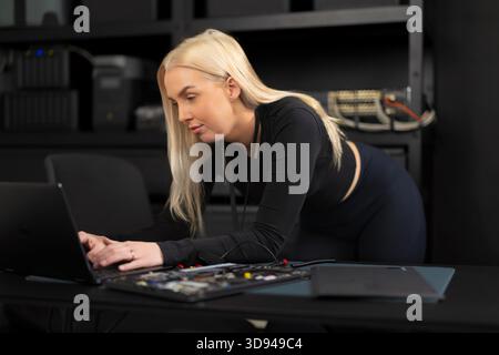 Female IT technician works on a laptop in a datacenter, performing diagnostics and troubleshooting Stock Photo