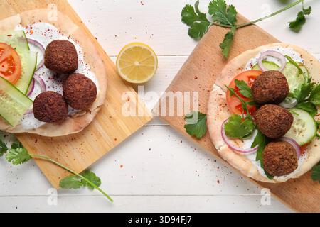 Cutting boards of delicious pitas with falafel and fresh vegetables on white wooden background Stock Photo