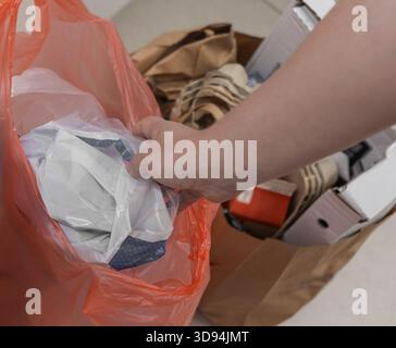 Close up vertical shot of hands placing a wrapped item into an orange plastic bag with blurred paper bags and boxes in the background Stock Photo