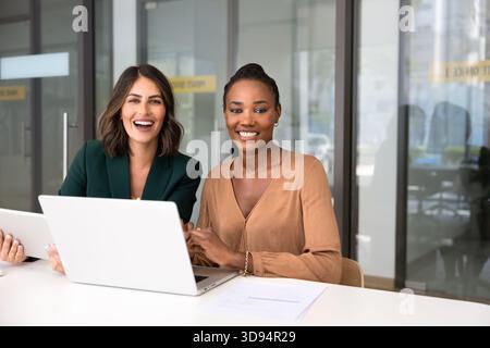 Two happy multiethnic female colleagues posing at workplace Stock Photo