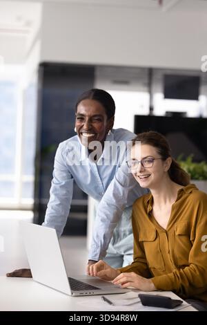 Happy joyful diverse female coworkers working together at laptop Stock Photo