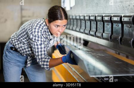 Young woman placing metal sheet on bending machine in workshop Stock Photo
