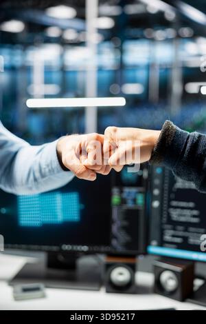 Close up of server farm IT coworkers doing fist bump after successfully deploying deep learning tools to automate tasks. Data center admins celebrating achievement, finishing AI training Stock Photo