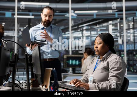 Engineering team doing brainstorming in data center, working together running scripts. Teamworking colleagues using programming language in server farm, finetuning network protocols Stock Photo