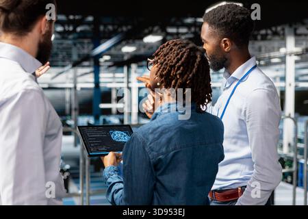 Team of admins manage diagnostics on tablet with system management tools to identify errors, doing brainstorming for optimization. Black engineers work together to prevent failure. Stock Photo